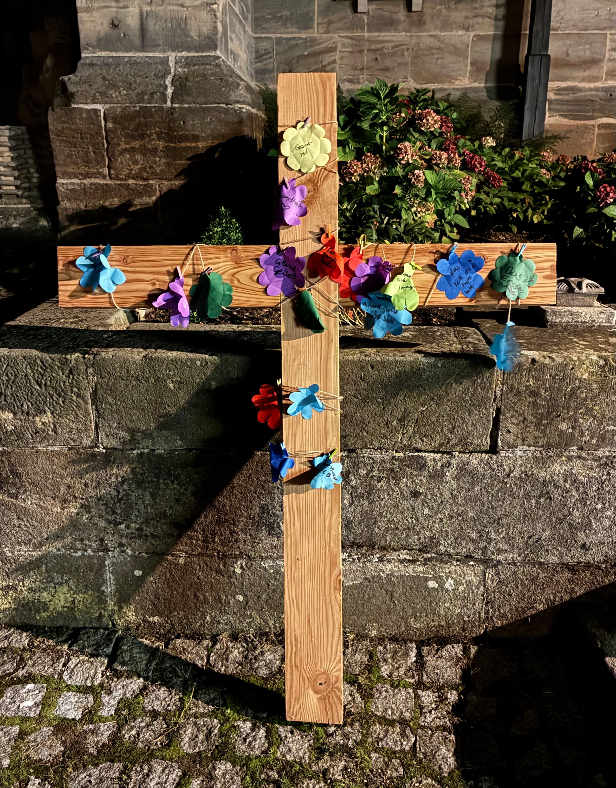 Zu sehen ist das Holzkreuz, an dem die aufgeblühten Papierblumen befestigt wurden.