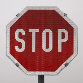 Rotes Stopschild mit weißer Schrift auf grauem Hintergrund.